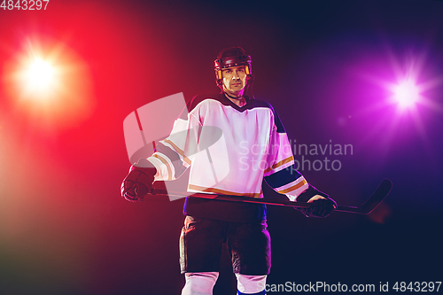 Image of Male hockey player with the stick on ice court and dark neon colored background