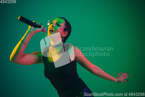 Image of Caucasian female singer portrait isolated on green studio background in neon light