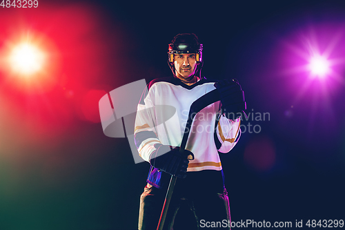 Image of Male hockey player with the stick on ice court and dark neon colored background