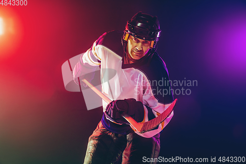 Image of Male hockey player with the stick on ice court and dark neon colored background