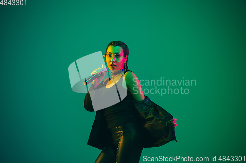 Image of Caucasian female singer portrait isolated on green studio background in neon light