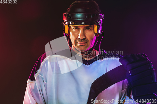 Image of Male hockey player with the stick on ice court and dark neon colored background