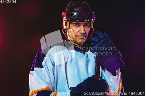 Image of Male hockey player with the stick on ice court and dark neon colored background