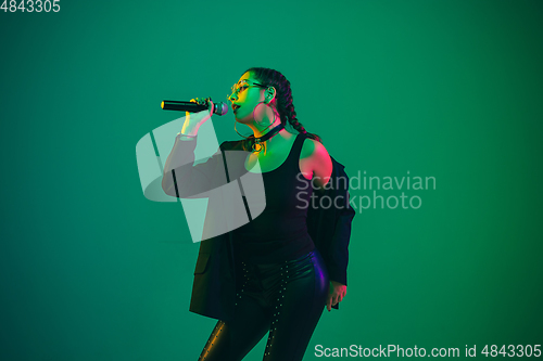 Image of Caucasian female singer portrait isolated on green studio background in neon light