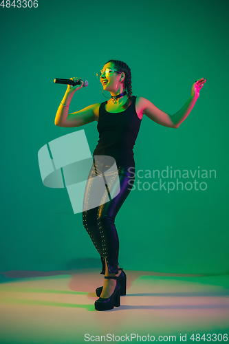 Image of Caucasian female singer portrait isolated on green studio background in neon light