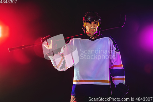 Image of Male hockey player with the stick on ice court and dark neon colored background