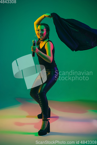 Image of Caucasian female singer portrait isolated on green studio background in neon light