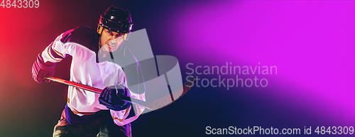 Image of Male hockey player with the stick on ice court and dark neon colored background