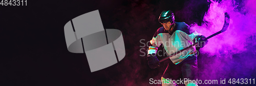 Image of Male hockey player with the stick on ice court and dark neon colored background