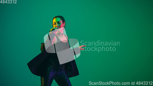 Image of Caucasian female singer portrait isolated on green studio background in neon light