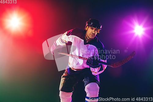 Image of Male hockey player with the stick on ice court and dark neon colored background