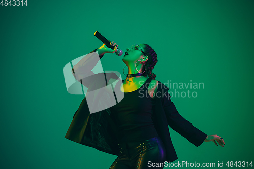 Image of Caucasian female singer portrait isolated on green studio background in neon light