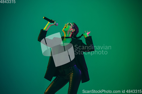 Image of Caucasian female singer portrait isolated on green studio background in neon light