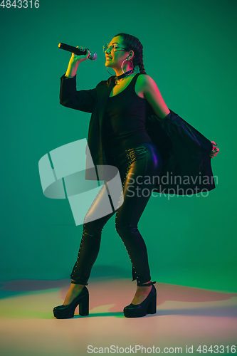 Image of Caucasian female singer portrait isolated on green studio background in neon light