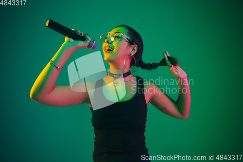 Image of Caucasian female singer portrait isolated on green studio background in neon light