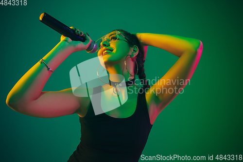 Image of Caucasian female singer portrait isolated on green studio background in neon light