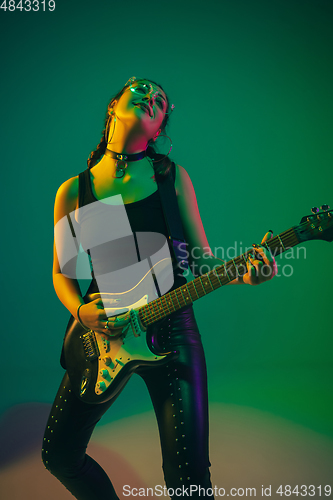 Image of Caucasian female guitarist portrait isolated on green studio background in neon light