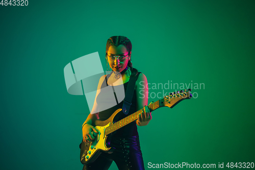 Image of Caucasian female guitarist portrait isolated on green studio background in neon light