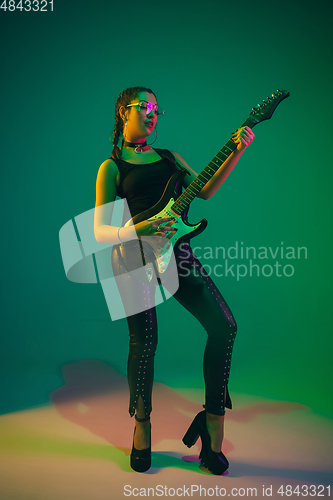 Image of Caucasian female guitarist portrait isolated on green studio background in neon light