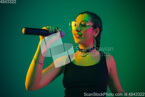 Image of Caucasian female singer portrait isolated on green studio background in neon light