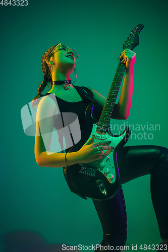 Image of Caucasian female guitarist portrait isolated on green studio background in neon light