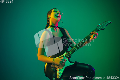 Image of Caucasian female guitarist portrait isolated on green studio background in neon light