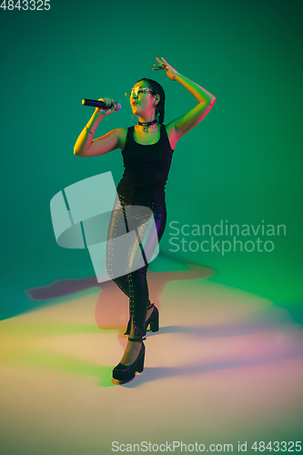 Image of Caucasian female singer portrait isolated on green studio background in neon light