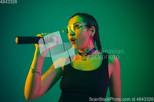 Image of Caucasian female singer portrait isolated on green studio background in neon light