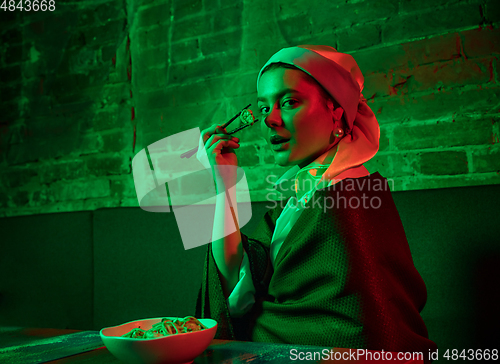 Image of Beautiful girl with a pearl earring taking lunch in modern cafe, restaurant in neon light