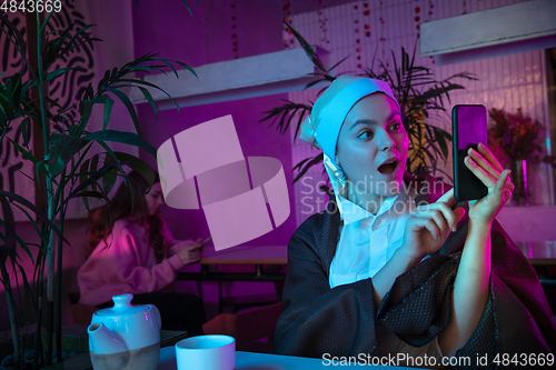 Image of Beautiful girl with a pearl earring taking lunch in modern cafe, restaurant in neon light