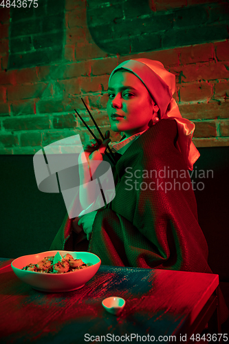 Image of Beautiful girl with a pearl earring taking lunch in modern cafe, restaurant in neon light