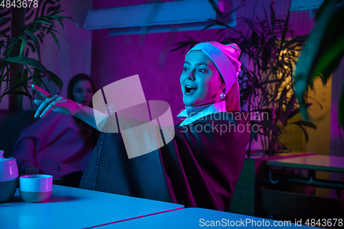 Image of Beautiful girl with a pearl earring taking lunch in modern cafe, restaurant in neon light
