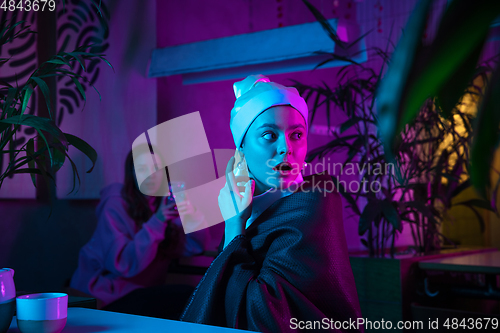 Image of Beautiful girl with a pearl earring taking lunch in modern cafe, restaurant in neon light