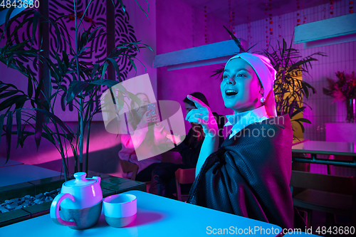 Image of Beautiful girl with a pearl earring taking lunch in modern cafe, restaurant in neon light