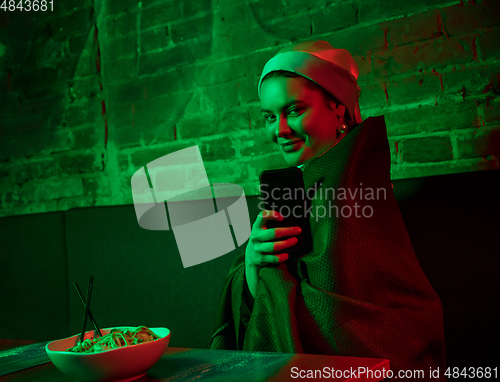 Image of Beautiful girl with a pearl earring taking lunch in modern cafe, restaurant in neon light