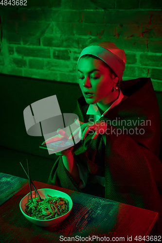 Image of Beautiful girl with a pearl earring taking lunch in modern cafe, restaurant in neon light