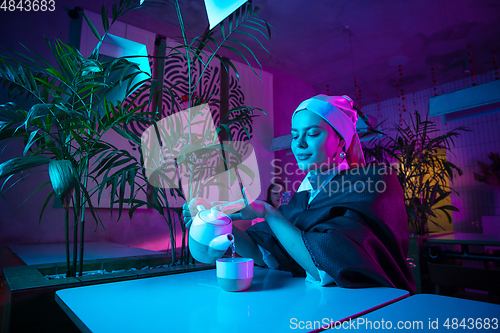 Image of Beautiful girl with a pearl earring taking lunch in modern cafe, restaurant in neon light