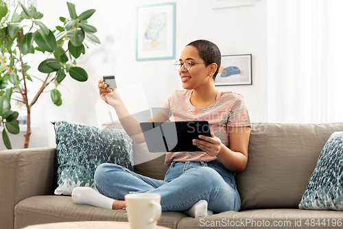 Image of happy woman with tablet pc and credit card at home