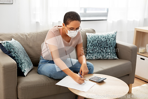 Image of woman in mask with papers and calculator at home