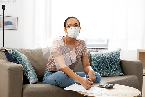 Image of woman in mask with papers and calculator at home