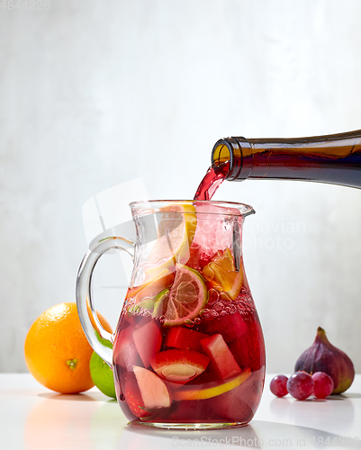 Image of red wine pouring into jug of cutted fruits