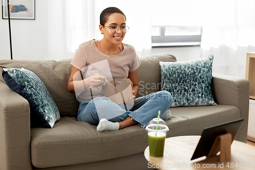 Image of african woman with tablet pc eating takeaway food