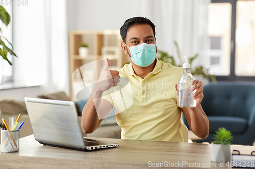 Image of man in mask with hand sanitizer at home office