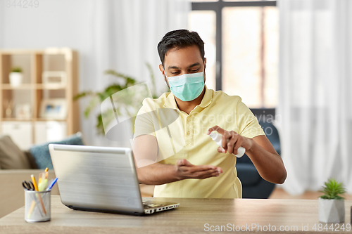 Image of man in mask using hand sanitizer at home office