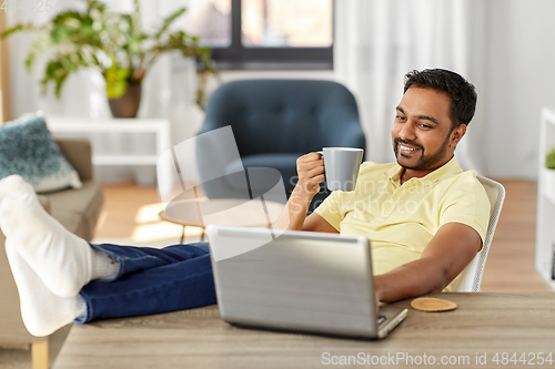 Image of man with laptop drinking coffee at home office