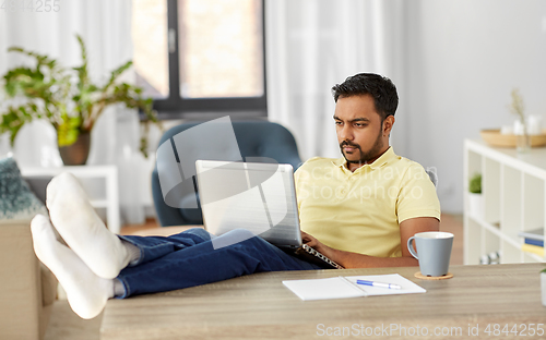 Image of man with laptop resting feet on table at home