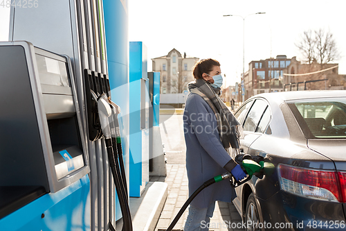 Image of woman in mask filling car at gas station