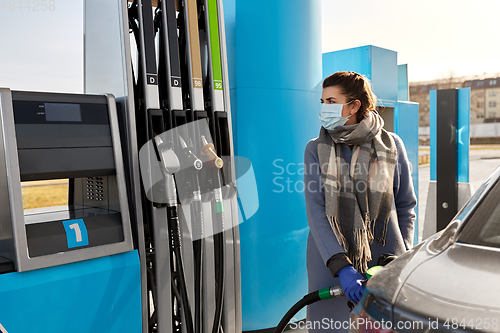 Image of woman in mask filling car at gas station