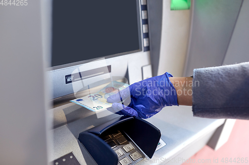 Image of hand in medical glove with money at atm machine