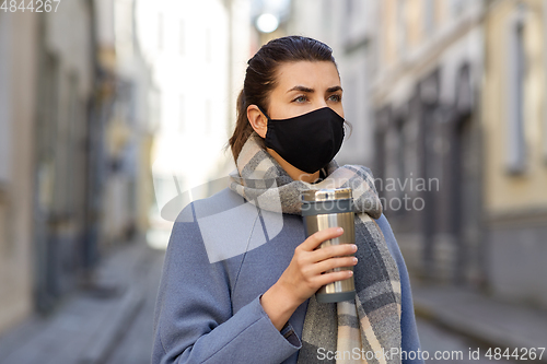Image of woman in reusable mask with tumbler in city